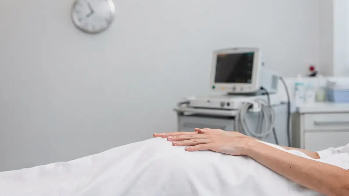 Klinisches Foto zu Geburtszeichen erkennen: Schwangere Hände in einer Geburtsstation mit Monitor und Bett